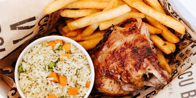 A tray with golden French fries, a piece of grilled chicken, and a cup of rice mixed with peas and carrots, served on printed parchment paper.