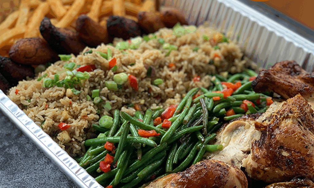 A tray filled with seasoned fries, fried plantains, fried rice topped with chopped green onions, sautéed green beans with red peppers, and roasted chicken pieces.