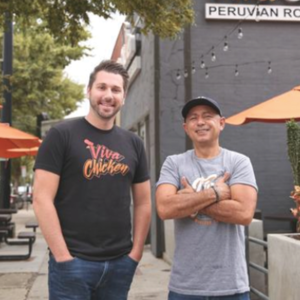 Two men stand smiling outside a restaurant with 