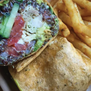 A close-up of a wrap filled with vegetables and possibly chicken, sliced open to show the colorful ingredients, served next to a portion of seasoned French fries.
