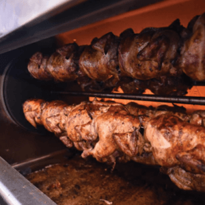 Whole chickens being roasted on a horizontal rotisserie inside an oven, with a golden-brown, crispy exterior forming on the meat.