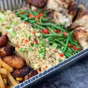 A tray filled with fried rice topped with chopped green onions, green beans, grilled chicken pieces, fried plantains, and French fries, arranged in separate sections.